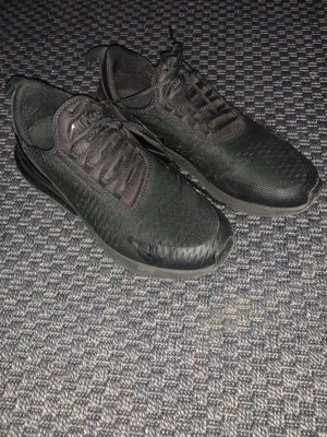 Svarta Nike 270s helsvarta - Säljer ett par helsvarta Nike Air 270s sneakers med mesh- och syntetmaterial. Skorna har en chunky sula med synlig luftbubbla i hälen, snörning och en sportig, modern look. Perfekta för dig som gillar stilrena och bekväma sneakers. Har ett litet hål som inte syns 