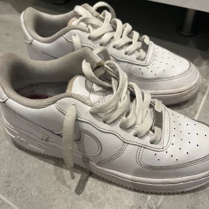 Nike Air Force 1 vita sneakers 36,5-37,5 - Klassiska vita Nike Air Force 1 sneakers i skinn med lågt skaft och snörning. Ikonisk design med perforerad tå och Nike-logga på sidan. Perfekta för dig som gillar streetstyle och vill ha en tidlös sneaker i garderoben. Storlek 36,5 men sitter lite större. Skorna är köpta på gallerian och lådan har jag inte hittat och det behövdes ett par sulor. Tveka inte på att fråga 
