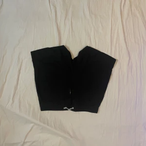 Svarta shorts med dragkedja - Svarta shorts med rak passform och dragkedja framtill. De har en enkel design med hällor för bälte och snörning i midjan. Perfekta för varma dagar när du vill ha en clean och stilren look.