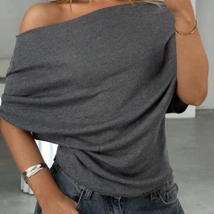 Mörkgrå offshoulder topp - Säljer en mörkgrå offshoulder topp i mjukt, ribbat material. Toppen har en lös passform och korta ärmar som sitter snyggt över ena axeln. Perfekt att styla med jeans för en chill och trendig look.❤️
