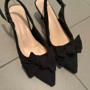 Svarta klackskor med rosett - Snygga svarta klackskor som är använda ca 3 gånger, storlek 39/40.