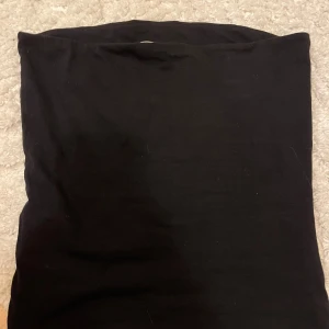 Svart enkel tube topp i bomull - Svart, rak och enkel tube topp i mjukt bomullstyg. Toppen har en minimalistisk design utan synliga detaljer eller mönster, perfekt för dig som gillar en clean och stilren look.