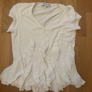 Vit volangblus från Cottonade - Supersöt vit blus från Cottonade med v-ringning och korta ärmar. Blusen har flera volangdetaljer. Jag har aldrig använt den men perfekt till vardags och fest. Storlek S 