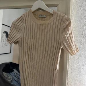 Beige ribbad topp från Zara Knit - Säljer en beige ribbad topp från Zara Knit i storlek S. Toppen har rund halsringning, korta ärmar och är figurnära i modellen. Materialet är stickat och stretchigt vilket gör den superbekväm. Perfekt att styla med jeans eller kjol för en clean look.