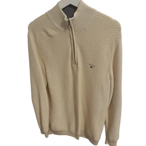Beige half zip tröja från Gant - Snygg beige tröja från Gant med strukturerat mönster och hög krage. Tröjan har half zip-dragkedja och diskret logga på bröstet. Perfekt för lager-på-lager och passar till både jeans och chinos.