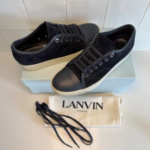 Lanvin skor  - Snygga marinblå sneakers från Lanvin med ovandel i mocka och tåparti i skinn. Skorna har rund tå, svarta snören och vit sula med diskret logga undertill. Kommer med Dustbag!! Uk 8 passar 42-43. Bara att höra av sig till oss vid minsta fundering😁