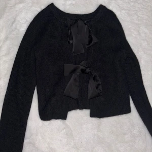 Svart stickad kofta med rosetter - Mysig svart stickad kofta med två stora satinrosetter framtill som stängning. Man kan ha den antingen fram eller bak. Personligen hade jag rosetterna bak. en söt touch till din outfit. Använd bara en gång samr köpt på nelly men står att den är från object.