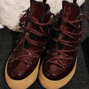 &Other Stories Vinröda moon boots med snörning storlek 37 - Snygga vinröda moon boots med glansig yta och grova röda snören. Skorna har en beige platt sula och svart foder på insidan. Perfekta för vintern med sin höga modell och coola look. Passar dig som vill sticka ut med ett par unika boots.