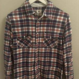 Rutig skjorta från Lee i bomull - Riktigt snygg rutig skjorta från Lee i bomull. Skjortan har blå, röda och vita rutor, två bröstfickor med knappar och klassisk krage. Perfekt för dig som gillar en avslappnad men ändå cool stil. Hör av dig vid frågor Mvh Oscar