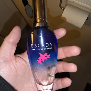 Escada Santorini Sunrise EdT 50ml - Limited edition parfym från Escada, Santorini Sunrise. Flaskan är elegant med blått till transparent glas och har en guldig kork. Dekorerad med rosa blommotiv och rymmer 50 ml eau de toilette. Kommer i en färgglad kartong med grekisk-inspirerat motiv.