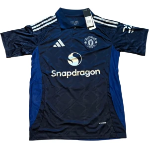 Manchester United Martinez bortatröja - Manchester United bortatröja med Martinez och nummer 6 på ryggen. Mörkblå med silvriga detaljer, broderat klubbmärke och Adidas-logga. Tillverkad i lätt och ventilerande Aeroready-material. Klassisk krage och korta ärmar. Perfekt för dig som älskar fotboll och United.