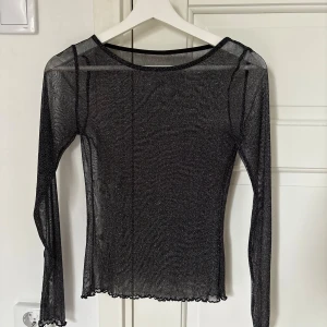Glittrig svart mesh topp/ festtopp - Säljer en transparent svart mesh topp med glittrigt tyg och långa ärmar.