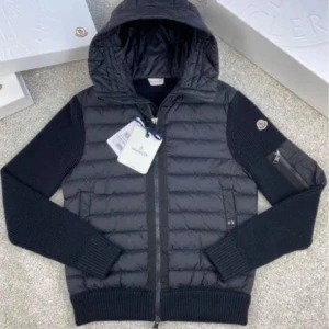 Svart Moncler cardigan  - Svart cardigan från Moncler i storlek 1 alltså S med stickade ärmar och vadderad kropp. Jackan har huva, dragkedja framtill, ribbade muddar och en praktisk ficka med dragkedja på ena ärmen. Klassisk Moncler-logga på ärmen och snygga detaljer 