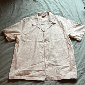 Beige kortärmad skjorta från SRNHLT - Snygg beige skjorta från SRNHLT i storlek 158. Skjortan har korta ärmar, klassisk krage och knäppning framtill. Tillverkad i mjukt linnematerial som ger en chill och luftig känsla. Perfekt för varma dagar och enkel att matcha med jeans eller shorts.