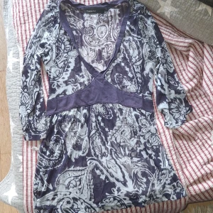 Mönstrad blus med v-ringning KappAhl - Supersnygg blus från KappAhl i marinblått och vitt med coolt paisleyinspirerat mönster. Djup v-ringning med markerad midja och trekvartsärm. Tunn och luftig, perfekt för dig som gillar unika prints och en feminin siluett.