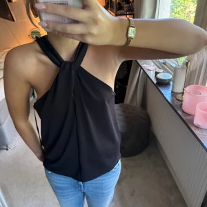 Svart halterneck Topp - Säljer en svart halterneck linnetopp med snygg knutdetalj framtill. Storlek M 