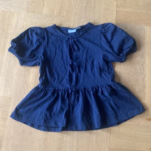 Mörkblå blus med puffärm Gina Tricot - Supersöt mörkblå blus från Gina Tricot med puffiga korta ärmar och volang nertill. Blusen har knyt framtill och är tillverkad i mjuk bomull. Perfekt för dig som gillar en feminin och trendig stil. Pris kan diskuteras 