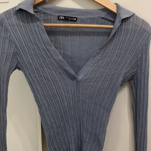 Ljusgrå ribbad tröja från Zara - Säljer en ljusgrå ribbad tröja från Zara med v-ringning och krage. Tröjan är långärmad och har en slim passform som sitter snyggt på kroppen. 