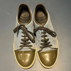 Lanvin sneakers i mocka och skinn - Snygga sneakers från Lanvin med blå mocka och olivgrön/grå blank tå. Skorna har rund tå med glansig tåhätta, svarta snören och beige/vit sula. Skorna kan absolut tvättas upp innan dem skickas och pris går att diskutera. Enda skönhets felet är en liten chip i hälen men inget man tänker på. 