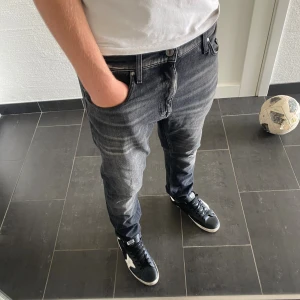 Tiger of Sweden - Snygga svarta jeans från Tiger of Sweden i modellen Pistolero. Jag är 185 och väger 77kg Jeansen har en tvättad look med ljusa slitningar och klassisk femficksdesign. De har normal passform och raka ben, perfekt för en avslappnad stil. Materialet är jeans och de har detaljerade sömmar och läderpatch bak.