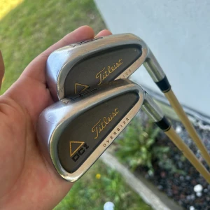 DCI Oversize 3 & 4 Järnklubbor - Två klassiska Titleist DCI Oversize järnklubbor (3 och 4) med snygg guldfärgad Tri-Spec-skaft. Perfekta för dig som vill ta ditt golfspel till nästa nivå och sticka ut på banan. Grepp med Titleist-logga för extra stil.