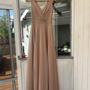 Champagnefärgad långklänning XXS - Glittrig champagnefärgad/ljusrosa långklänning från bubbelroom i omlottmodell med v-ringad hals.  Klänningen har en elegant siluett med dragkedja i ryggen och har även en slits längs vänstra benet. Aldrig använd bara testad en gång. (Etikett kvar) Perfekt för dig som ska på ett bröllop eller tar studenten och ska gå balen.