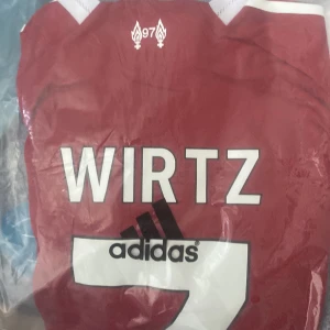 Adidas fotbollströjor Gyökeres & Wirtz - Två officiella Adidas fotbollströjor: en vit med vinröda detaljer och Gyökeres 11-tryck, samt en vinröd med vita detaljer och Wirtz-tryck. Båda har klassisk passform, tryckta namn och nummer samt klubbemblem. Perfekta för dig som vill visa support för dina favoritspelare.