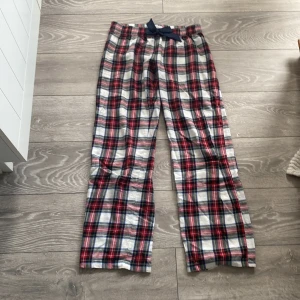 Rutig byxa med rosett från Gina Tricot - Snygga rutiga byxor från Gina Tricot i vitt, rött, blått och svart. Byxorna har en midjeresår och en marinblå rosett framtill. Tillverkade i mjuk bomull, perfekta för chill dagar. Rak passform och klassiskt rutmönster ger en avslappnad vibe.