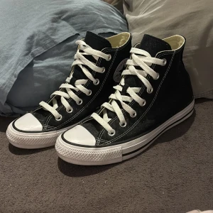 Svarta Converse Chuck Taylor All Star - Klassiska svarta Converse Chuck Taylor All Star high-tops med vit tå och vita snören. Använda ett par gånger på gym inomhus. Dem är lite dammiga pga att jag inte använt dom på länge men det går att fixa! 