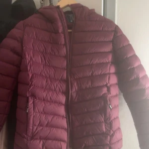 Vinröd pufferjacka från Vinson Polo Club - Säljer en vinröd pufferjacka från Vinson Polo Club i storlek S. Jackan har huva med dragsko, två fickor med dragkedja och ett emblem på ärmen. Perfekt för kyliga dagar och har en snygg, sportig look.