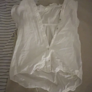 Vit v-ringad skjorta i linne - Säljer en luftig vit skjorta i linne med v-ringning och knappar framtill. Skjortan är ärmlös och har en avslappnad passform, perfekt för varma dagar. Enkel och stilren design som är lätt att matcha.