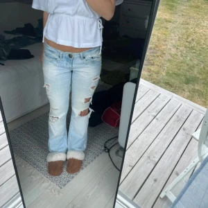 Ljusblå slitna bootcut jeans Coquette - Säljer ett par ljusblå bootcut jeans från Coquette med flera slitningar och hål på benen. Jeansen har låg midja och klassisk femficksmodell. Perfekta för dig som gillar en avslappnad och trendig look. Midjemått är ungefär 38 och innerbensmåttet är ungefär 76🥰