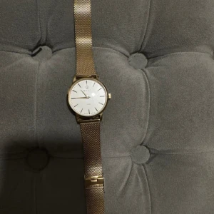 Guld klocka från Gant med meshband - Stilren klocka från Gant med guldigt mesharmband i rostfritt stål och vit urtavla. Klockan har minimalistisk design med tunna index och klassisk rund form. Perfekt accessoar för dig som gillar en clean och modern look.