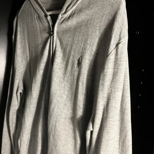 Grå kofta från Polo Ralph Lauren - Snygg grå kofta från Polo Ralph Lauren med dragkedja framtill och klassisk logga broderad på bröstet.