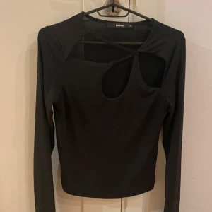 Svart långärmad topp med cut-outs Bikbok - Svart långärmad topp från Bikbok med unika cut-out detaljer framtill och asymmetrisk halsringning. Snygg och trendig design som sticker ut, perfekt för dig som gillar att experimentera med din stil. Mjuk och stretchig känsla.