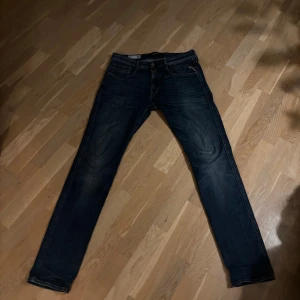 Replay Anbass mörkblå jeans - Snygga mörkblå Replay Anbass jeans med klassisk femficksdesign och raka ben. Jeansen har diskreta slitningar och detaljerade sömmar, tillverkade i mjukt denimtyg som sitter skönt. Perfekta för dig som gillar en stilren och modern look.