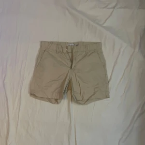 Beige shorts med dragkedja - Snygga beige shorts med klassisk passform och dragkedja framtill. Perfekta för varma dagar och enkla att matcha med det mesta. De har fickor på sidorna och är tillverkade i ett mjukt bomullstyg.
