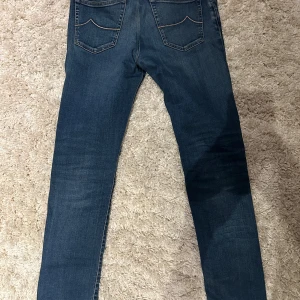 Blå jeans från Jacob Cohën - Snygga blå jeans från Jacob Cohën med klassisk femficksdesign och raka ben. Jeansen har en mörk tvätt med lätt slitning och kontrastsömmar på bakfickorna. Perfekta för dig som gillar en stilren och tidlös look.
