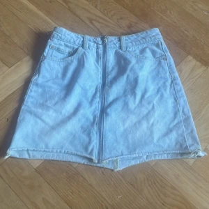 Ljusblå jeanskjol med dragkedja XS - Säljer en ljusblå jeanskjol från BikBok i storlek XS. Kjolen är kort, har en snygg silverfärgad dragkedja framtill med rund ring, bälteshällor och klassiska fickor både fram och bak. Perfekt för dig som gillar denim och vill ha en cool detalj i garderoben.