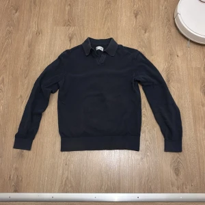 Mörkblå stickad pikétröja - Snygg mörkblå stickad pikétröja från These glory days med klassisk krage och lång ärm. Tröjan har diskret struktur i materialet och ribbade muddar vid ärmslut och nederkant. Perfekt för en stilren och avslappnad look.