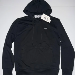Svart CDG Hoodie - Svart hoodie från Comme des Garçons Play med klassiskt hjärta med ögon broderat på bröstet. Tröjan är helt ny och har inga spår av defekter eller skador.