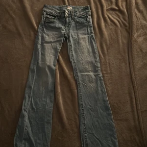 Blå bootcut jeans från Gina Tricot - Snygga ljusblå jeans från Gina Tricot i modell 158. Jeansen har klassisk femficksdesign, dubbla knappar i midjan och bootcut-ben som ger en retrovibe. Perfekta att styla med sneakers eller boots. Materialet är mjukt denim i bomull.