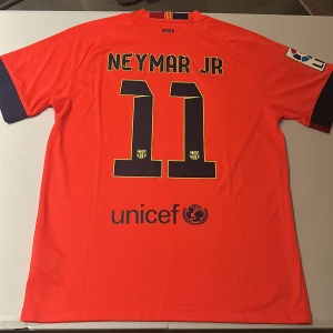 FC Barcelona Neymar Jr matchtröja - Snygg FC Barcelona fotbollströja med Neymar Jr och nummer 11 på ryggen. Tröjan är röd med mörkblå detaljer, officiella klubbmärket, La Liga-patch och Qatar Airways-tryck. Tillverkad i lätt Dri-FIT-material som andas, perfekt för match eller träning. Replika, endast handtvätt gäller!