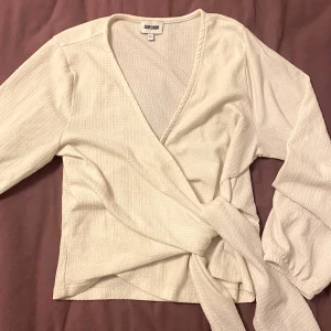Vit topp från Bubbleroom med knytt, XS - En vit topp från Bubbleroom med knyt i storlek XS. Toppen har långa ärmar med resår vid ärmslut, v-ringning och knytband i midjan. 