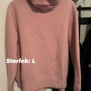 Rosa polotröja med pärldetaljer strl: L - Mysig rosa polotröja med pärldetaljer runt halsen. Tröjan är stickad och har lång ärm samt ribbade muddar. Perfekt för dig som gillar en söt och trendig look under kyliga dagar. Förekommer noppor.