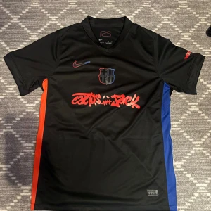 FC Barcelona Lamine Yamal/ Travis scott Nike fotbollströja/ÄKTA!! - Snygg svart FC Barcelona fotbollströja från Nike med Lamine Yamal och nummer 19 på ryggen. Tröjan har röda och blå detaljer på sidorna, klubbmärke på bröstet och Dri-FIT-material som andas. Tryck med Cactus Jack och UNHCR-logga. Perfekt för dig som älskar Barca.