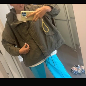 Olivgrön loose vindjacka med snörning - Säljer en olivgrön vindjacka med loose passform och coola snörningsdetaljer i nederkant. Storlek S från Zara