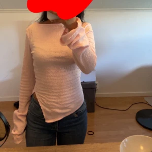 Ljusrosa långärmad topp med struktur - Säljer en ljusrosa långärmad topp med strukturerat tyg och asymmetrisk nederkant. Toppen har en tight passform och är tillverkad i ett stretchigt material som sitter snyggt på kroppen. Perfekt för dig som gillar en enkel men ändå unik stil.