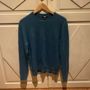Blå Cashmere tröja från Uniqlo - En stilren blå Cashmere tröja från Uniqlo i storlek S. Tröjan har rund halsringning, långa ärmar och ribbade muddar vid ärmslut och nederkant. Perfekt för lager-på-lager och enkel att matcha med jeans eller kjol.