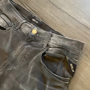 Replay Grover grå jeans, raka ben - Snygga Replay Grover jeans i tvättad grå färg med raka ben och klassisk femficksdesign. Byxorna har en guldfärgad knapp och Replay-logga vid fickan. Tillverkade i mjukt jeanstyg som ger en avslappnad vibe.